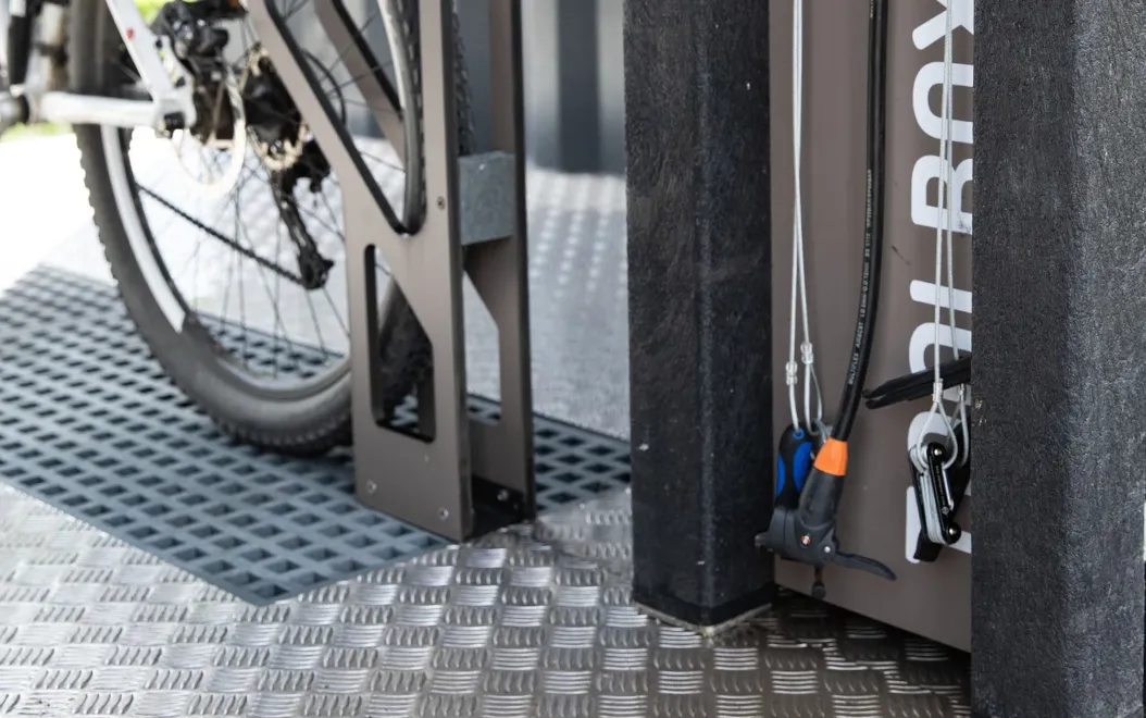 Detalhe de bomba de ar e ferramentas da tool box da bike station high tech floema personalizada, com vista parcial do suporte para bicicletas e grelha de recolha de águas residuais.