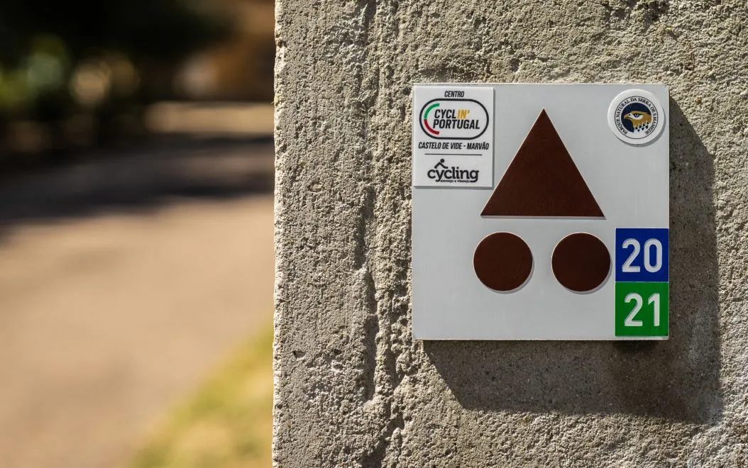 Detalhe de placa de base Centros Cyclin' Portugal com autocolantes de percurso e de homologação, instalada em parede.