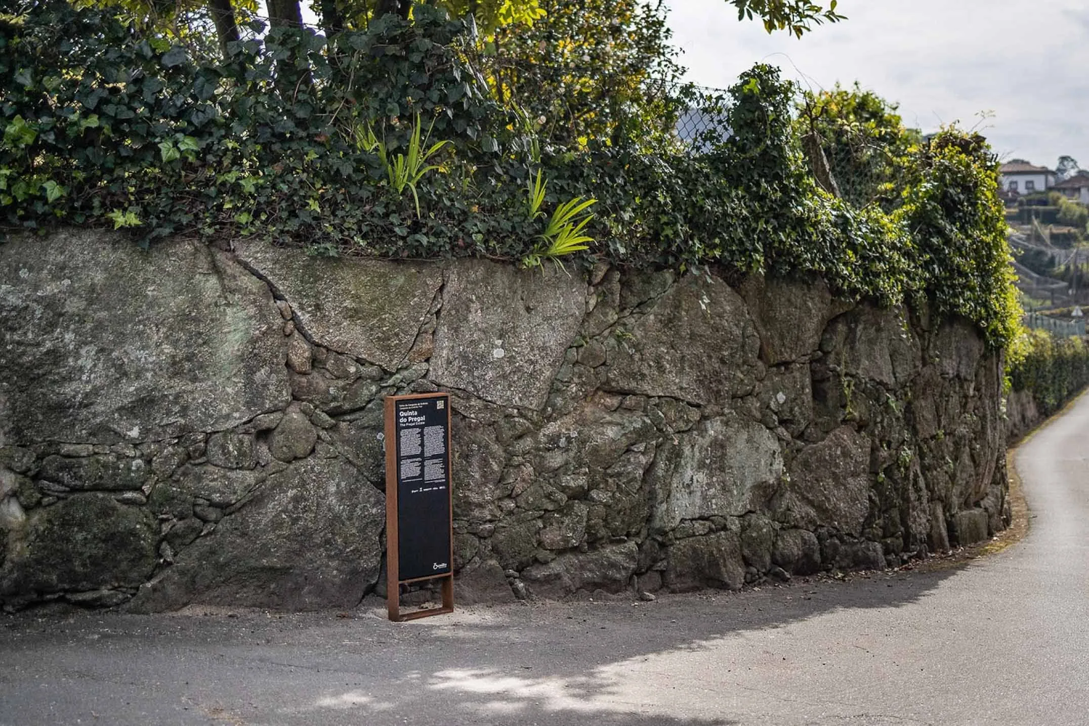 Totem informativo Frame, da Floema, com estrutura em aço corten e painel em HPL+ encostado a muro de pedra em ambiente rural.