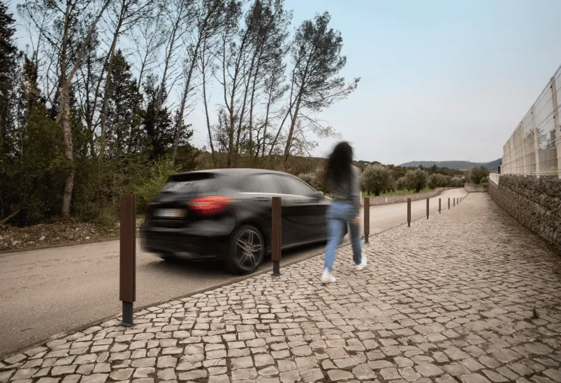 Rua com carro e mulher a caminhar no passeio com pilaretes Floema Frame em plástico reciclado.