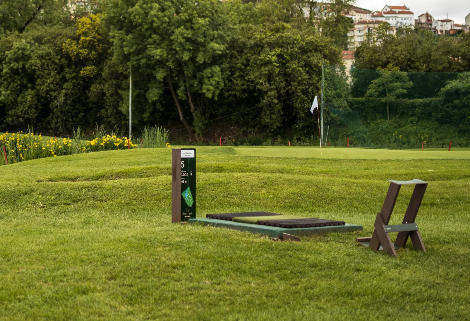 Vista de campo de golfe com zona de tee de campo de golfe, com sinalética personalizada e bag stand royal da Floema. Estruturas produzidas em plástico reciclado castanho e HPL+.