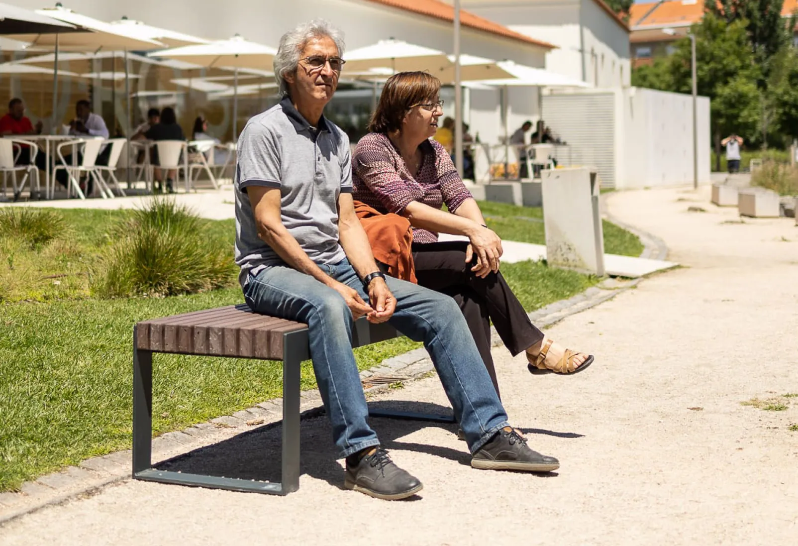 Casal sentado no banco sem encosto da coleção Frame da Floema num parque urbano.