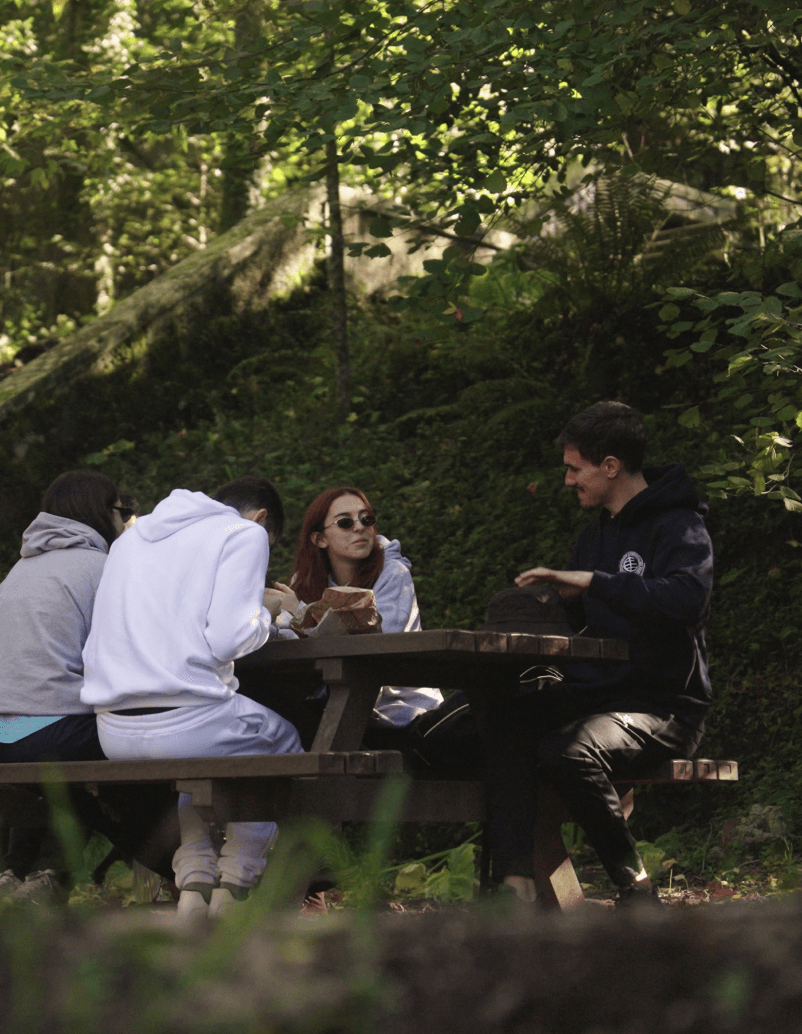 Personas sentadas y conversando en un parque natural, en una mesa de pícnic de plástico reciclado marrón, modelo Floema.