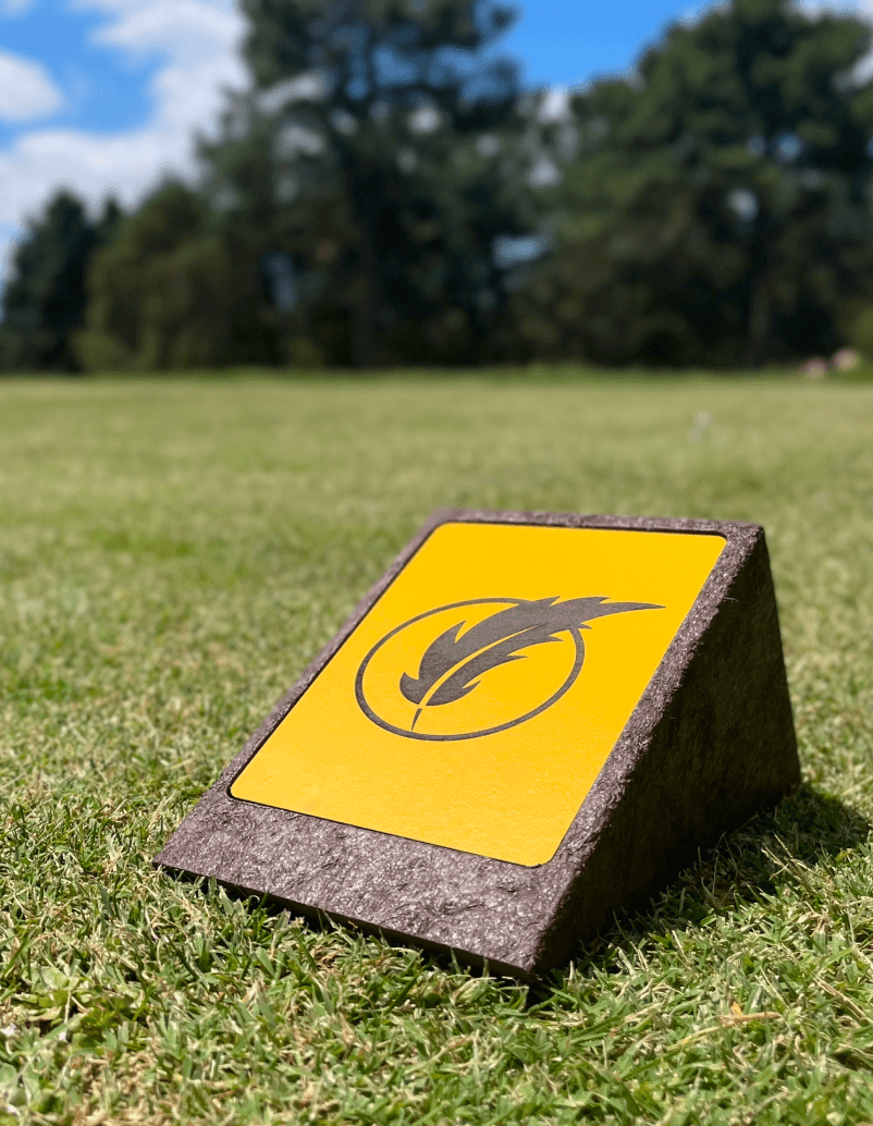 Detalle de log marker en zona de tee de campo de golf. Con estructura en plástico reciclado marrón y logotipo grabado a láser en HPL.