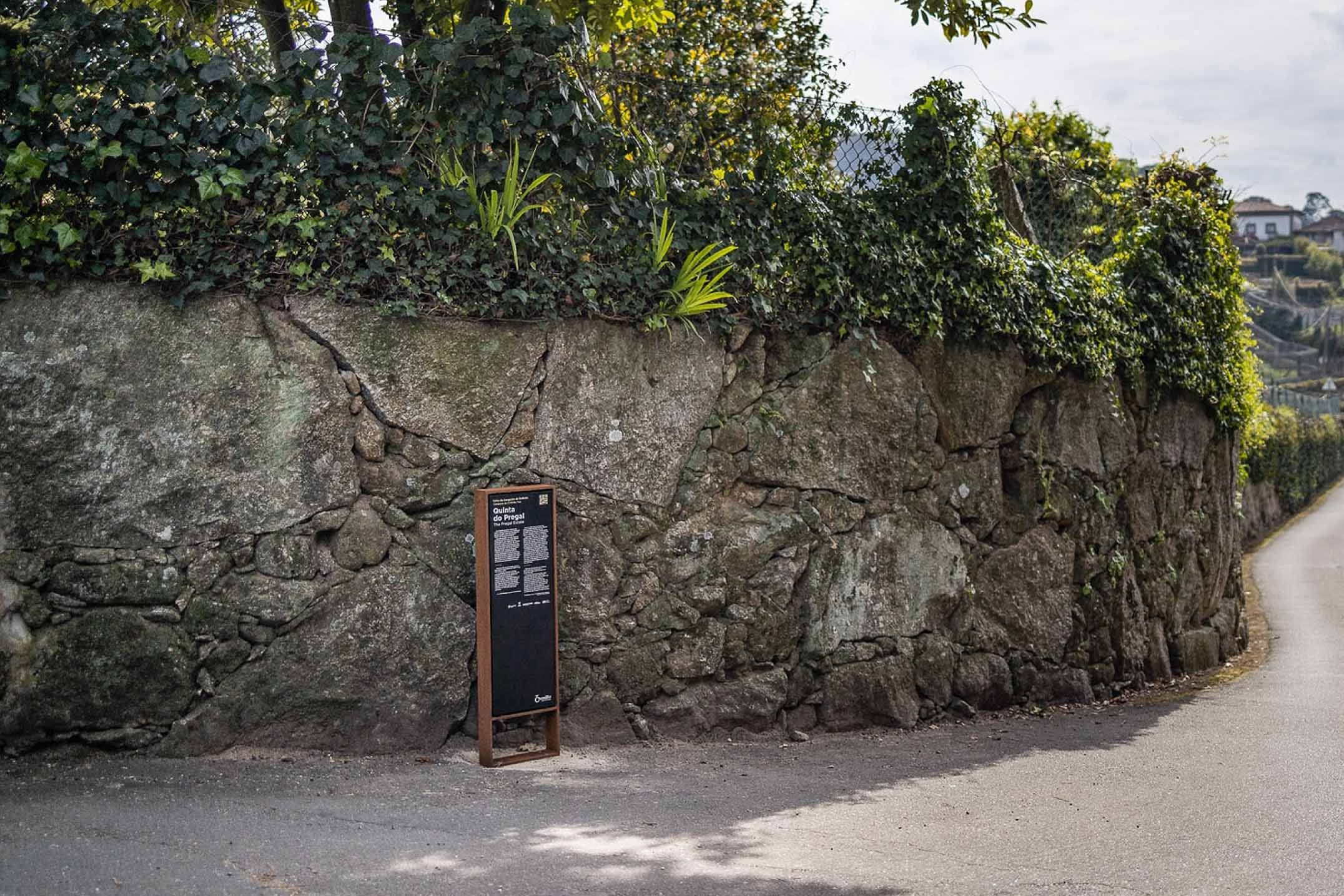 Tótem informativo Frame, de Floema, con estructura de acero corten y panel en HPL+ adosado a un muro de piedra en un entorno rural.