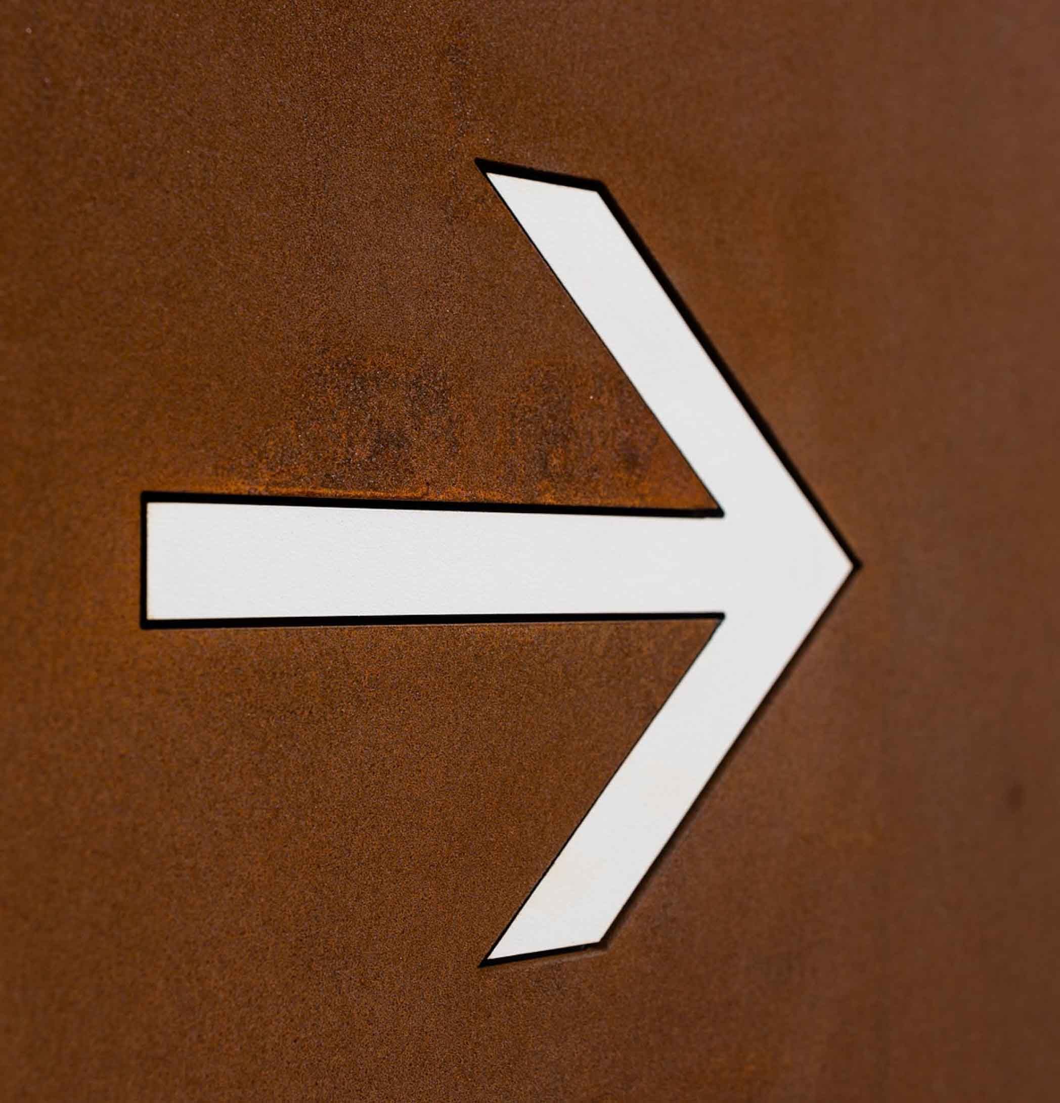 Detalle de flecha calada con negativo en HPL en tótem direccional personalizado en acero corten para ruta urbana.