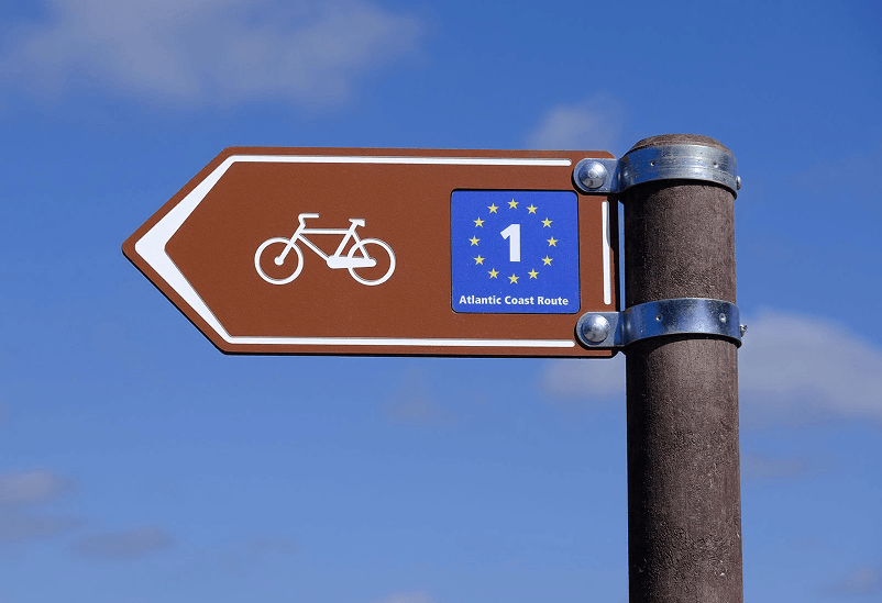 Placa direccional de rutas ciclistas en HPL+ con personalización para la ruta EuroVelo. Incluye poste de plástico reciclado marrón y sistema de fijación con abrazaderas de acero inoxidable.