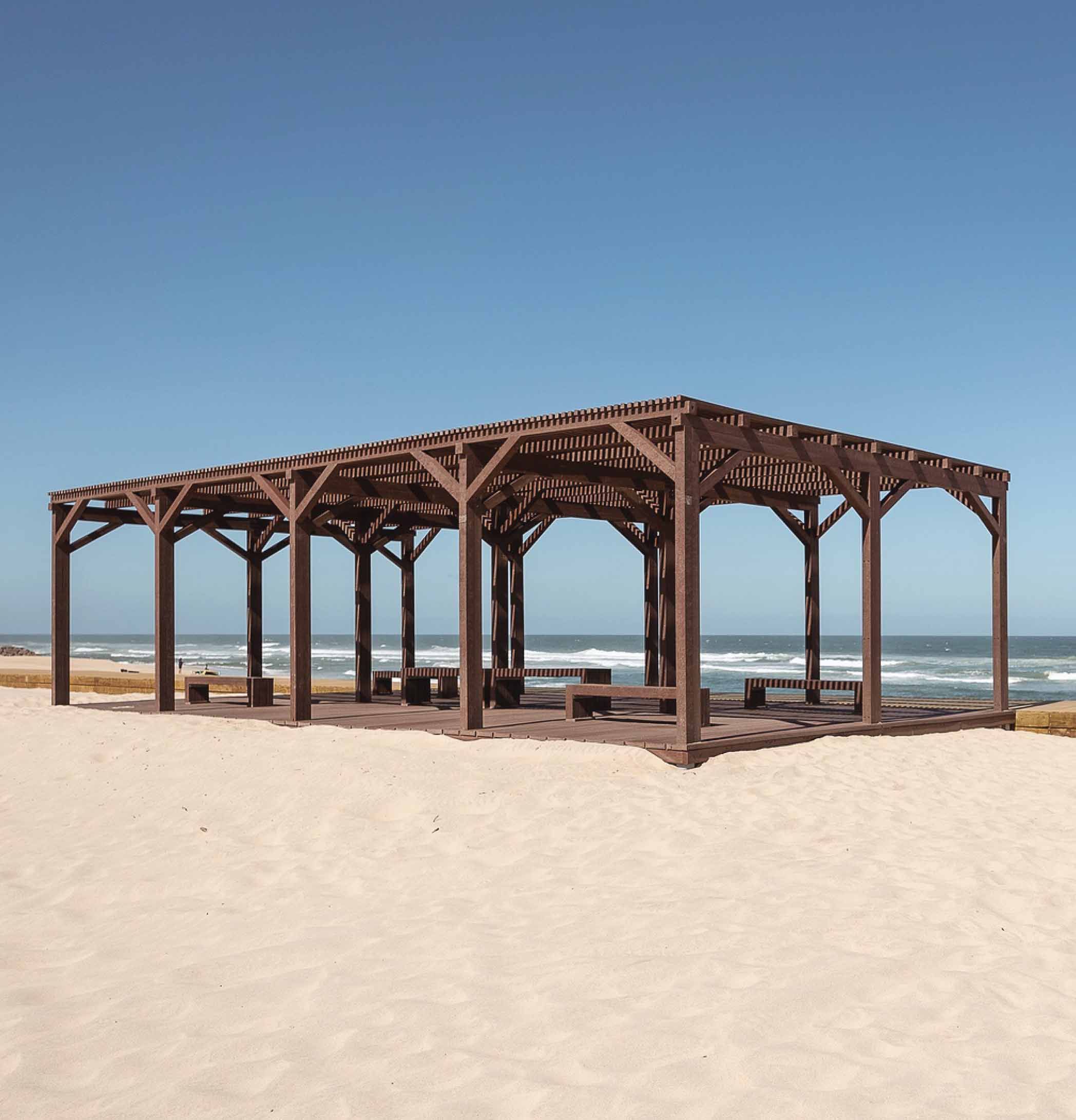Pérgola de plástico reciclado marrón Floema con bancos de plástico reciclado en la playa.