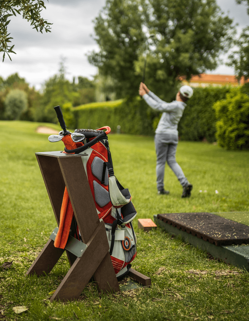 Vista lateral del bag stand Royal de Floema en plástico reciclado marrón y HPL+, con bolsa para palos de golf. Jugador de golf en momento de swing.