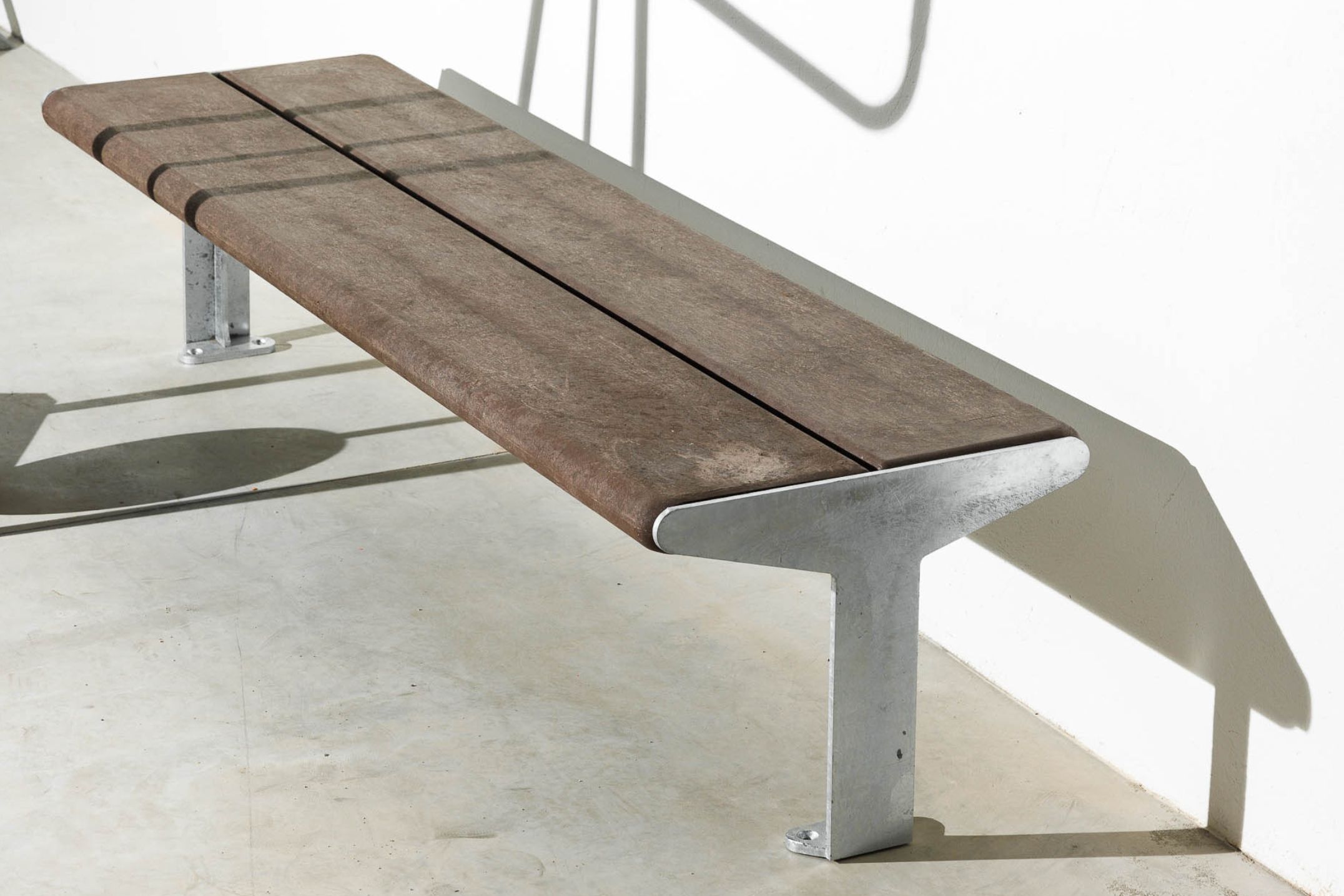 Banco sin respaldo de la línea Reuse, colección Floema Urban, con estructura de acero galvanizado y tablones de plástico reciclado marrón.