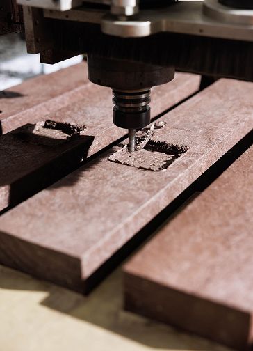 CNC milling machine carving a rectangular groove into dark wooden planks