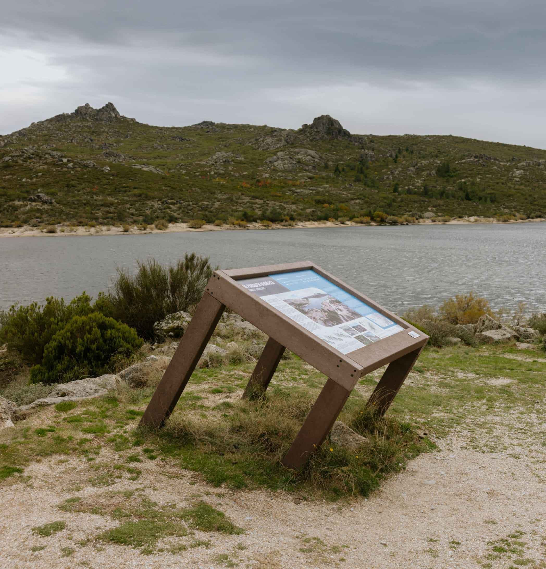 Mesa interpretativa ICNF en plástico reciclado Floema en un valle de la Serra da Estrela, con una laguna y montañas al fondo.