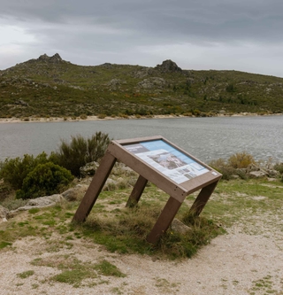 Mesa interpretativa ICNF de plástico reciclado Floema en un valle de la Serra da Estrela, con una laguna y montañas al fondo.