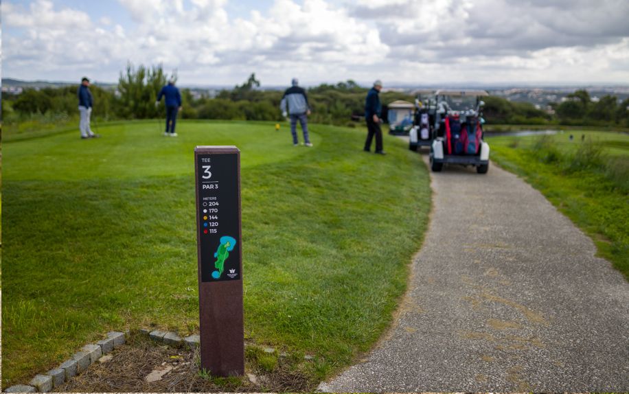 Vista general de la zona de tee de un campo de golf con jugadores y foco en el tee totem royal de floema en plástico reciclado marrón y HPL+.