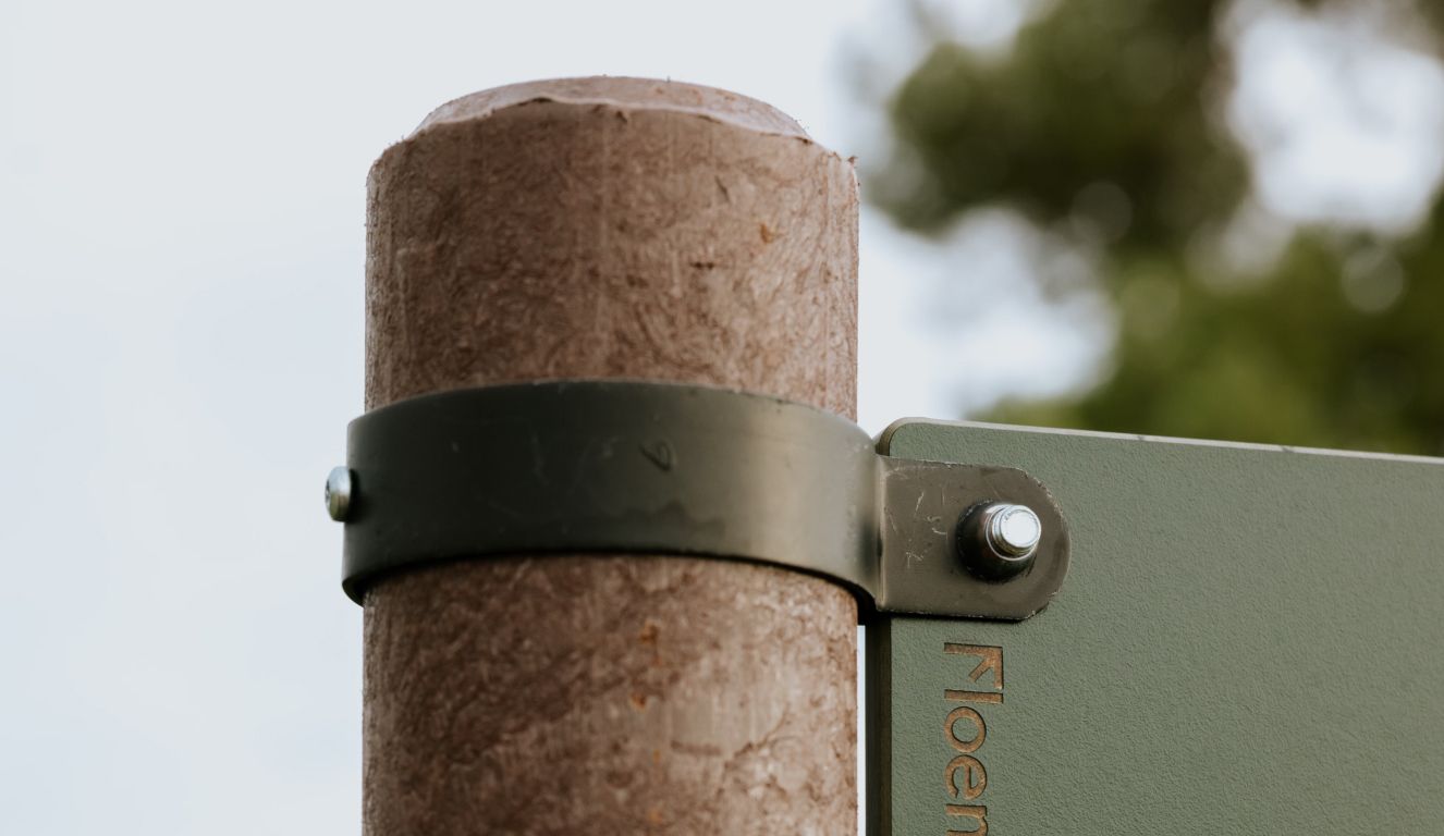Detalle de poste en plástico reciclado marrón Floema y de abrazaderas como sistema de fijación de placa direccional de recorridos peatonales en HPL+.
