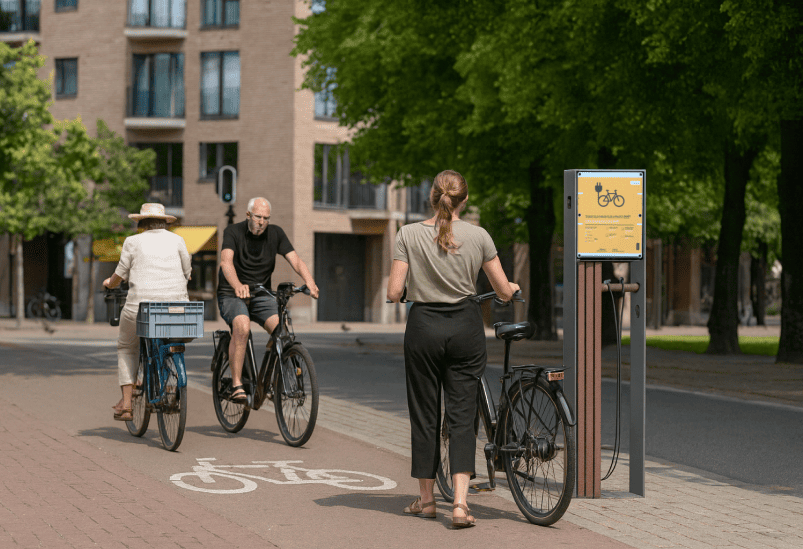 Una calle con personas en bicicleta y un cargador para bicicletas eléctricas de Floema, fabricado en plástico reciclado, junto al carril bici.
